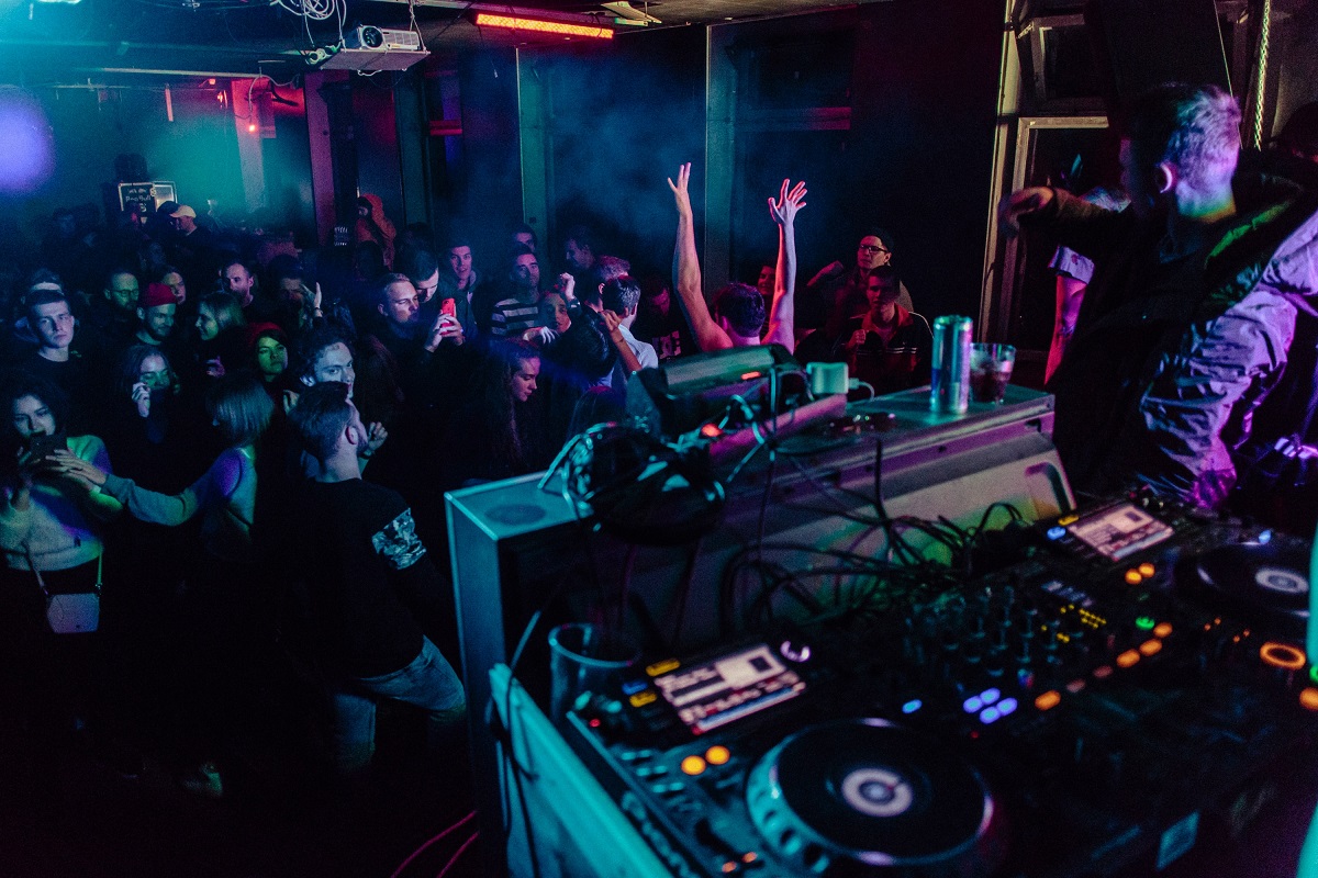 photo of a DJ booth at a club with a crowd of people watching