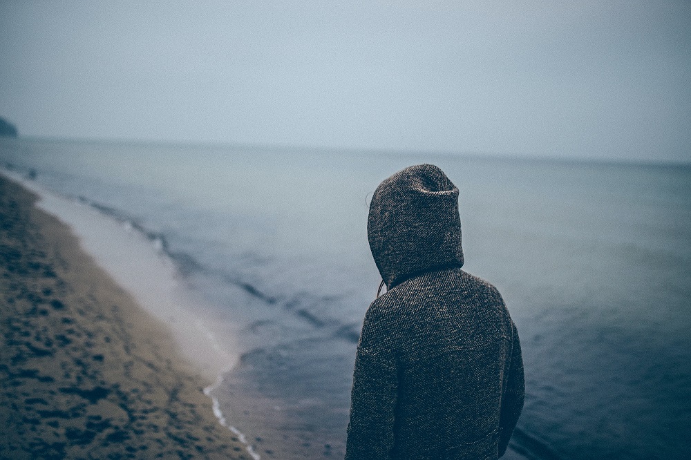 photo of a person wearing a hoodie walking along a beach