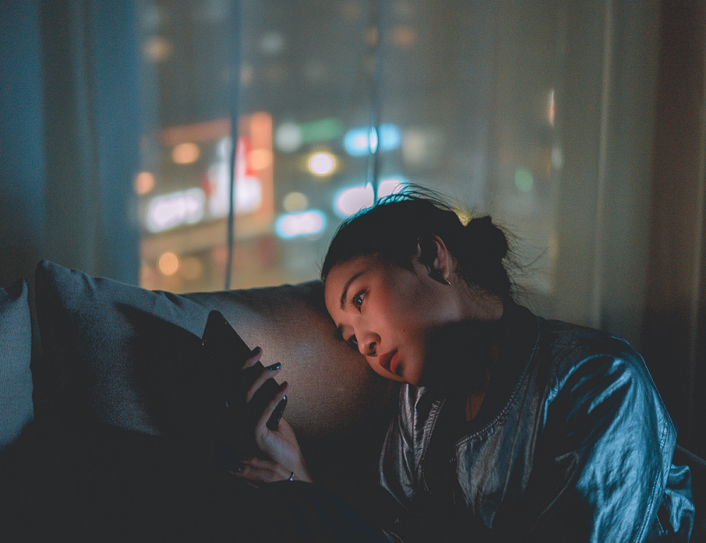 photo of a woman sitting on a couch alone looking at her phone