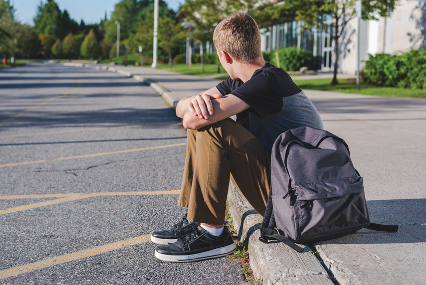 Stock photo of a teen boy sitting on a curb