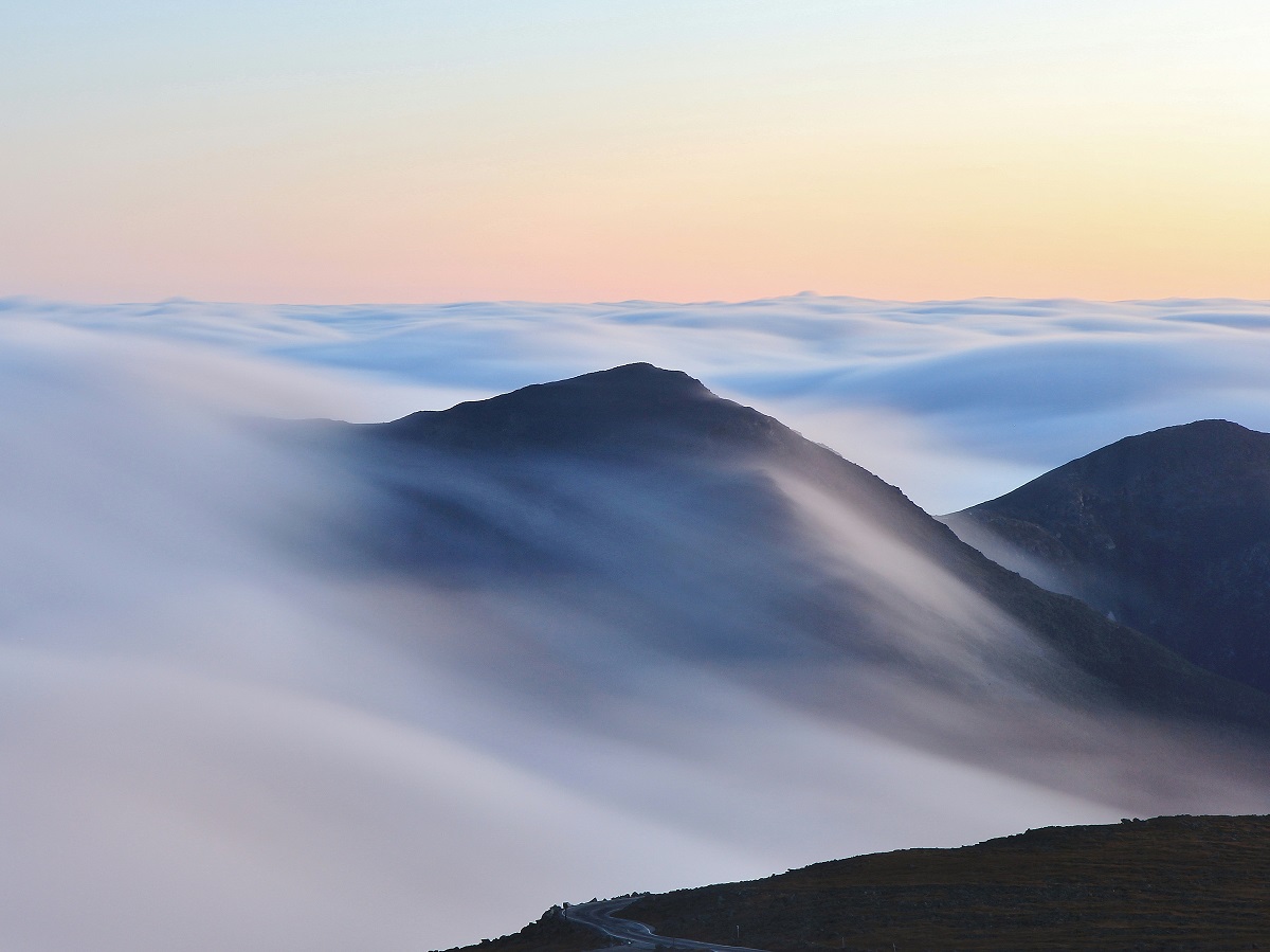 photo of fog moving over a low mountain