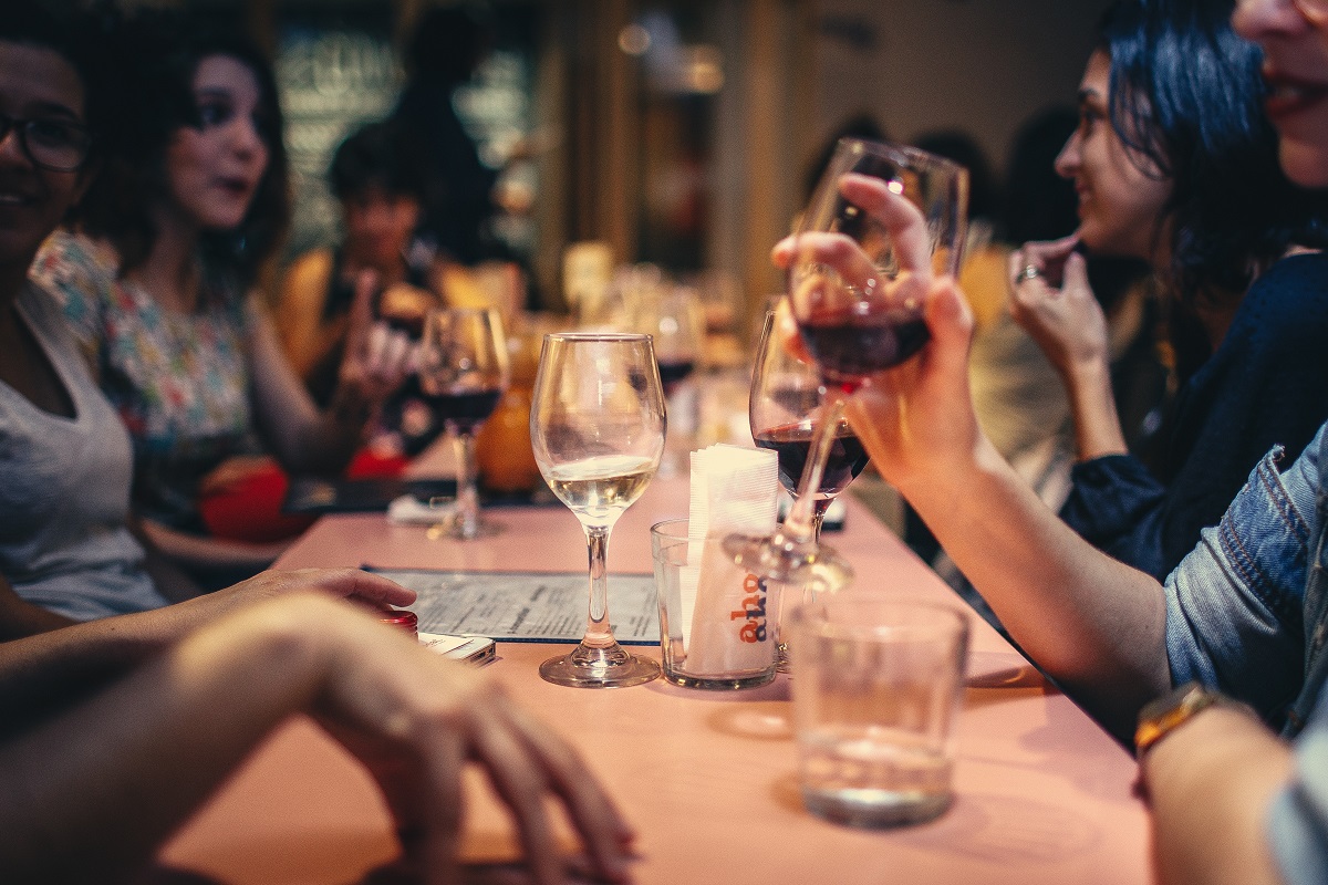 stock photo of a group of people at a restaurant table. Some of them are drinking wine.
