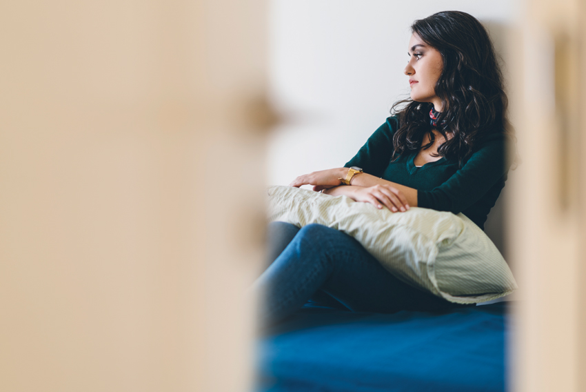 Stock photo of sad young woman sitting on her bed